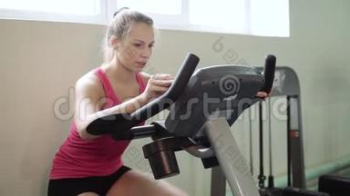 年轻漂亮的女孩在健身房里，在自行车模拟器上摇晃着她的腿。理念：热爱运动，去健身房，适当的